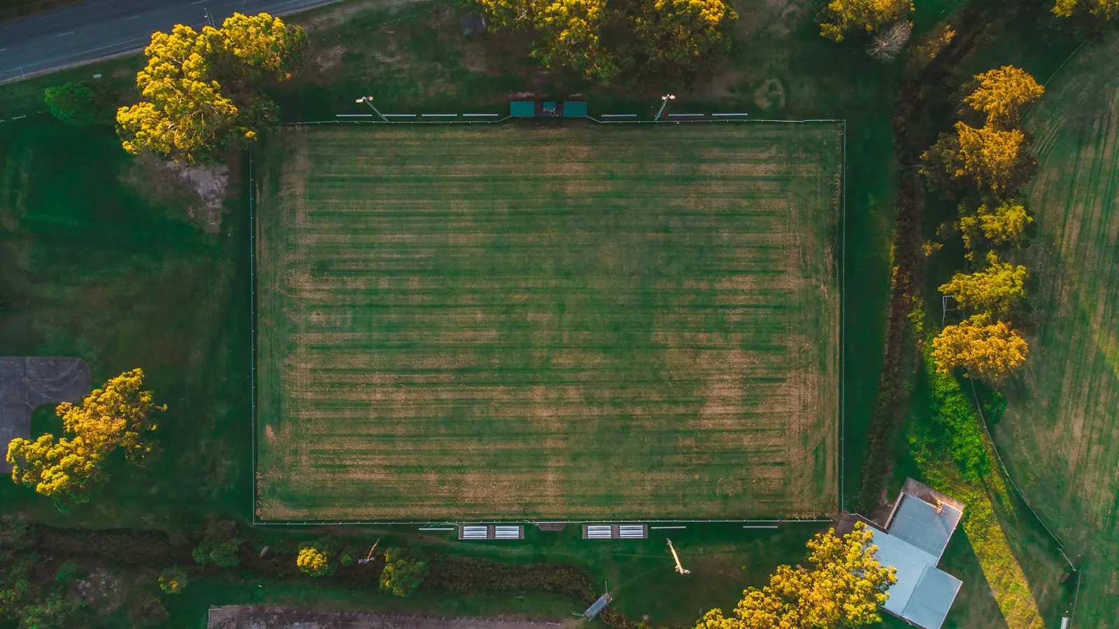 Aerial view of a grass football field surrounded by trees at sunset