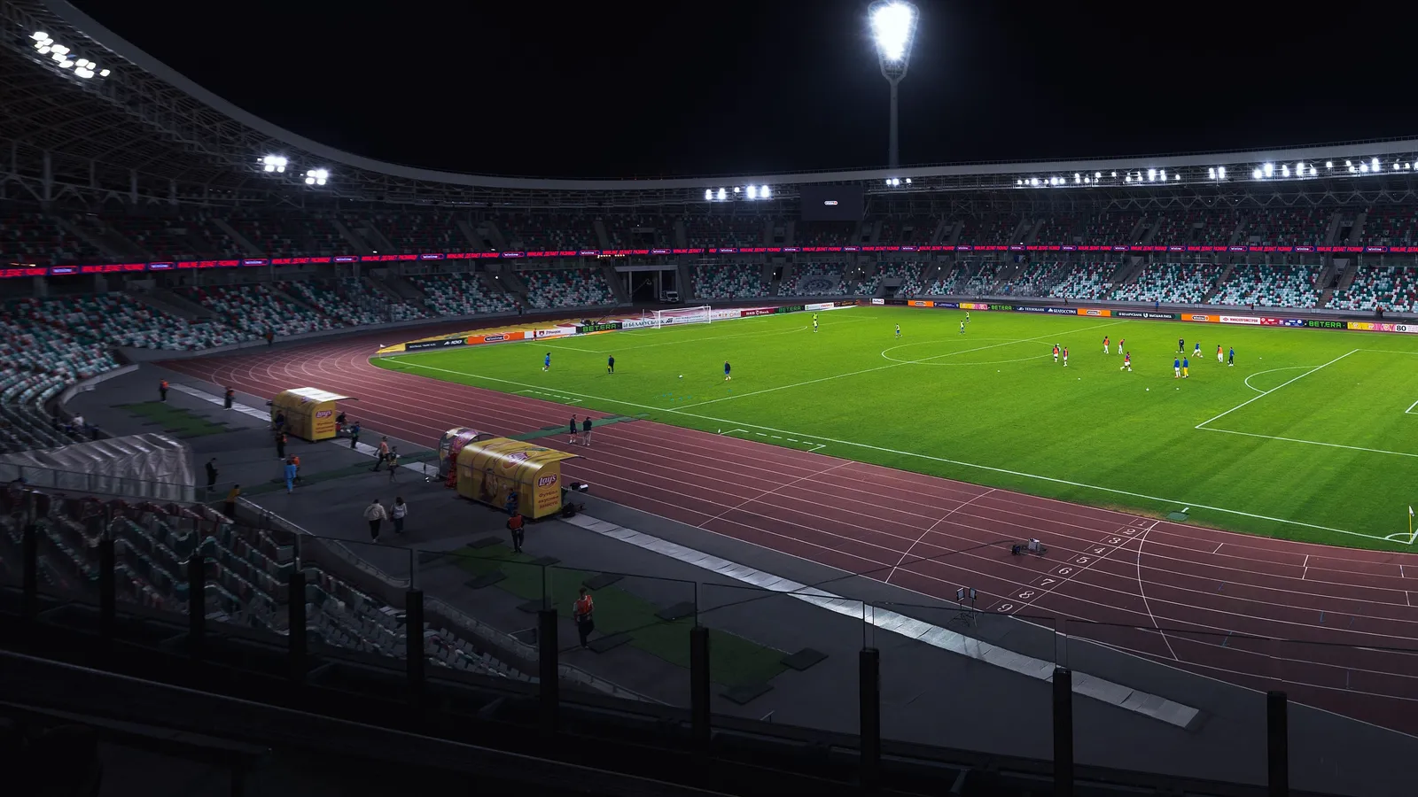 Floodlit football stadium at night with a match under way on a green pitch